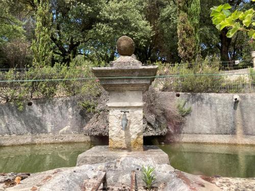 a stone fountain in the middle of a pond at La Viste - SPA-JACUZZI - MASSAGE- SAUNA - 4 SAISONS - Piscine Chauffée Toute l'année - Heated POOL - 800m City Centre in Nyons