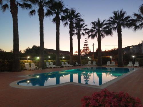 a pool with palm trees and chairs at dusk at Villa Laura Residence Hotel Apartments & Studios in Ascea