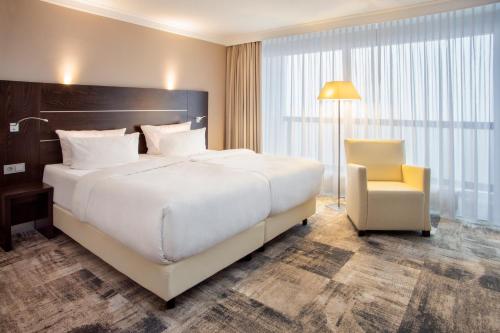 um quarto com uma grande cama branca e uma cadeira em Mercure Hotel Lüdenscheid em Lüdenscheid