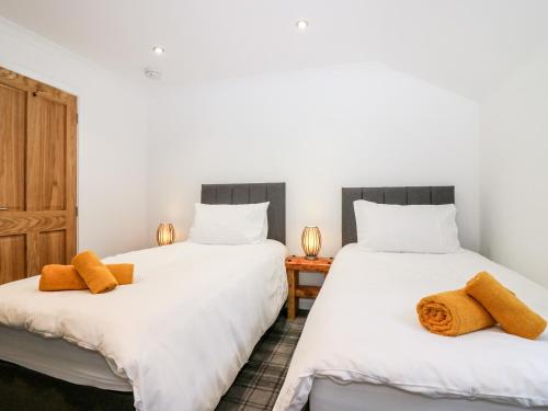 2 camas en una habitación con sábanas blancas y toallas naranjas en The Keepers Cottage at The Institute Executive Apartments en Keith