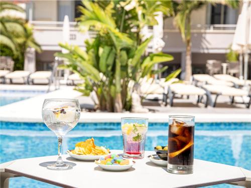 貝尼多姆的住宿－洛斯阿拉莫斯酒店，一张桌子,旁边放着食物和饮料盘,在游泳池边