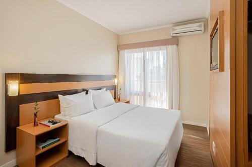 una habitación de hotel con una gran cama blanca y una ventana en Piazza Navona Porto Alegre by Intercity, en Porto Alegre