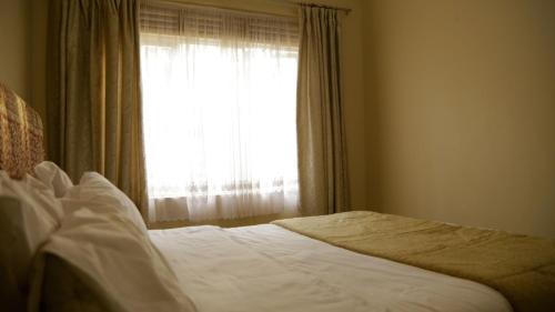 a bedroom with a white bed with a window at Kaz Breeze Gardens in Kampala