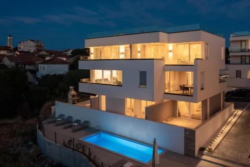 a large white house with a swimming pool at night at Luxury Apartment Dreams in Okrug with swimming pool, sea view, Wifi, parking in Trogir
