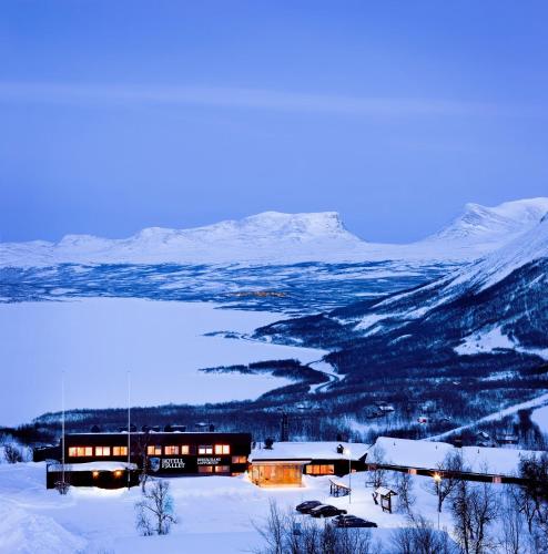 a building in the snow with mountains in the background at Hotell Fjället in Björkliden