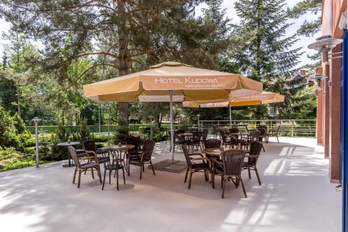a patio with tables and chairs under an umbrella at Hotel Kudowa Manufaktura Relaksu in Kudowa-Zdrój