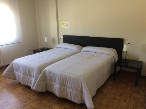 una camera con due letti con lenzuola bianche di Pensión Avenida a O Pedrouzo