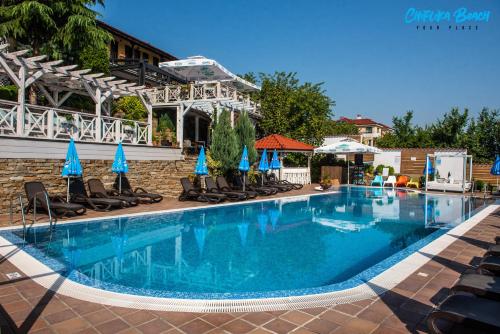 a large swimming pool with chairs and blue umbrellas at Chiflika Family Hotel in Asenovgrad