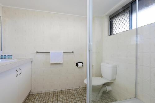a bathroom with a toilet and a glass shower at Wunpalm Motel & Cabins - Late check-in available in Maroochydore