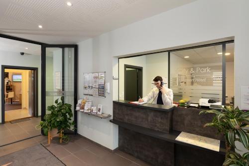 a man talking on a cell phone behind a counter at The Originals Residence, Kosy Appart'hotels Troyes City & Park in Troyes
