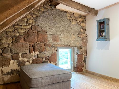 a room with a stone wall with a couch and a window at La Belle Petite Ferme Rosiers de Julliac 19350 in Les Bos