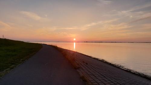 a path next to a body of water with the sunset at Chalet Buutengeweun, met luxe JACUZZI en TONSAUNA in Sint Annaland