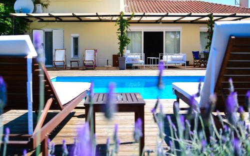 a patio with chairs and a swimming pool with purple flowers at Serenity Luxury Villa, Skiathos in Agia Paraskevi