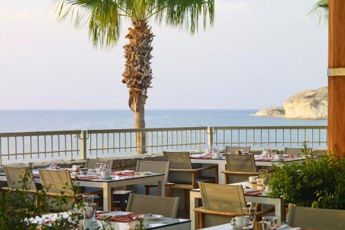 a restaurant with tables and a palm tree and the ocean at Columbia Beach Resort in Pissouri