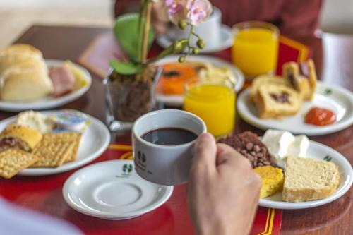 uma pessoa segurando uma xícara de café em uma mesa com alimentos para o pequeno-almoço em Hotel Nacional Inn São Carlos & Convenções em São Carlos