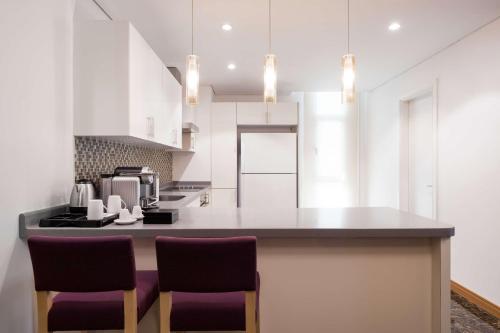 a kitchen with white cabinets and a counter with chairs at SAS Residence & Hotel Dhahran in Al Khobar