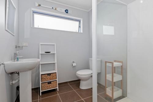 a white bathroom with a toilet and a sink at Pohutukawa Peace - Mangawhai Holiday Home in Mangawhai