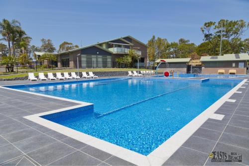 a swimming pool with white chairs and a house at BIG4 Easts Beach Holiday Park in Kiama
