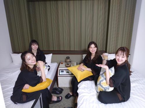 four women sitting on beds in a hotel room at Hotel Area One Oita in Oita