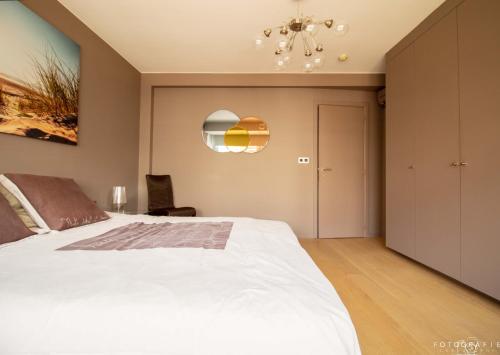 a bedroom with a large white bed and a chandelier at Zeezicht Sibeac Koksijde in Koksijde