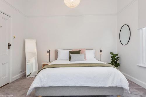ein weißes Schlafzimmer mit einem großen Bett und einem Spiegel in der Unterkunft Best on Regent, Central location, LUX 3bdm in Sandy Bay