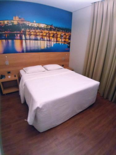a bedroom with a white bed with a painting on the wall at Hotelog in Campina Grande do Sul