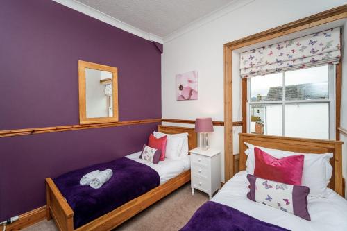 zwei Betten in einem Schlafzimmer mit einer lila Wand in der Unterkunft Bridge Cottage in Keswick