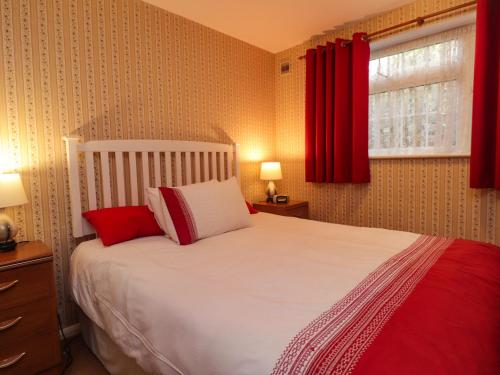 a bedroom with a white bed with red curtains at Old Post Office in Ashford