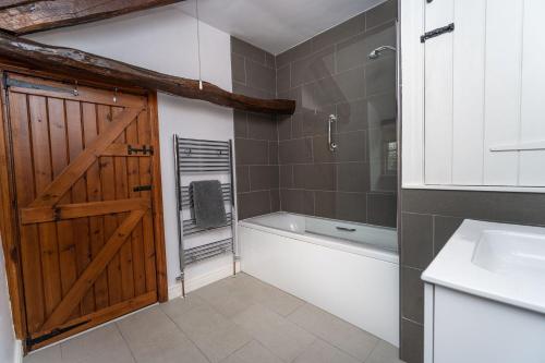a bathroom with a wooden door and a tub and a sink at Jasmine Cottage in Portinscale