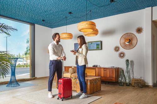 a man and woman standing in a living room with a suitcase at Ibis Styles Montpellier Aéroport Parc Des Expos in Mauguio