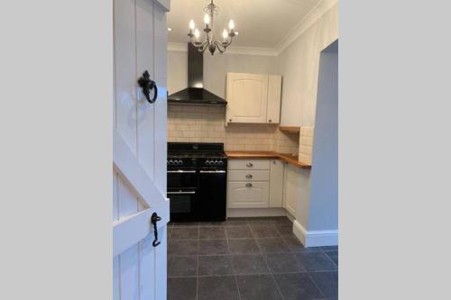 a kitchen with white cabinets and a black stove at Garden Suburbs Cottage in Crosskeys