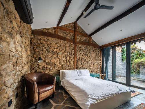 a stone walled bedroom with a bed and a leather chair at Brickyard Retreat at Mutianyu Great Wall Adjoin to Mutianyu Great Wall - Room with the View of Great Wall - Chinese massage experience - Vehicle Shuttle Service - International Catering - SPA& Nail Beauty Facilities in Huairou