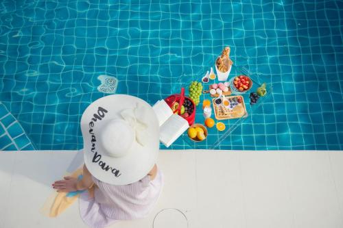 un bambino che indossa un cappello seduto in piscina di Dhevan Dara Resort & Spa Hua Hin - Pool Villa a Hua Hin