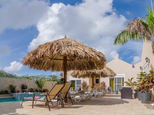 a group of chairs and a large straw umbrella at Golden Villas in Palm-Eagle Beach