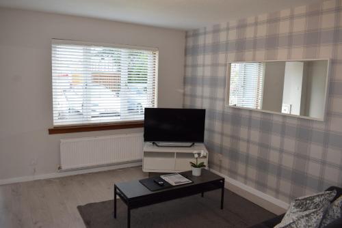 a living room with a tv and a table at Kelpies Serviced Apartments- Jamieson in Stenhousemuir