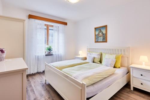 a white bedroom with a bed and a window at Apartmenthaus Haringer in Novacella