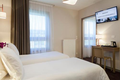 a hotel room with two beds and a desk and a window at Nehô Suites Porte de Genève - Gare Annemasse in Annemasse