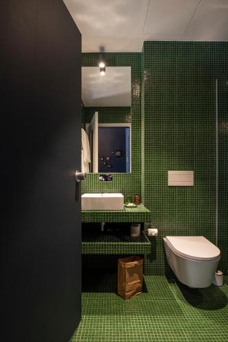 a green tiled bathroom with a toilet and a sink at toctoctoc lisboa in Lisbon