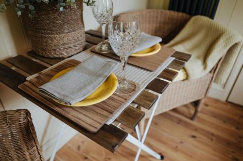 a wooden table with plates and wine glasses on it at The Shepherds Huts & The Well Lodge at Ormesby Manor in Ormesby Saint Michael