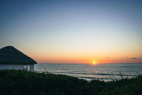 a house on the beach with the sunset in the background at Kumba Lodge in Praia do Tofo
