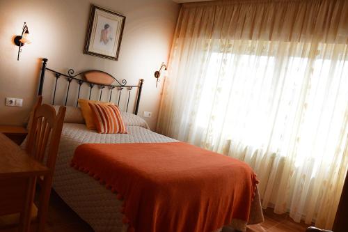 a bedroom with a bed with an orange blanket and a window at Pensión Quilmes in Vimianzo
