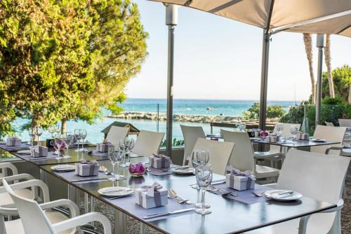 a restaurant with tables and chairs with the ocean in the background at Crowne Plaza Limassol by IHG in Limassol