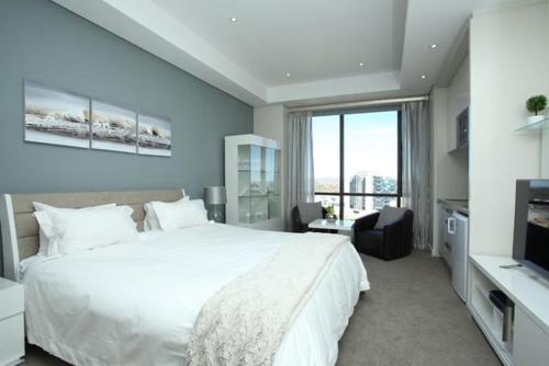 um quarto com uma grande cama branca e uma televisão em Sandton Skye Exclusive Apartment em Joanesburgo