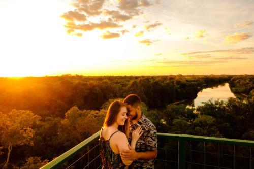a man and a woman standing on a balcony with the sunset at Hotel Pantanal Mato Grosso in Poconé