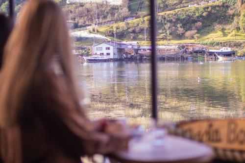 a woman sitting at a table looking at a lake at Palafito Hospedaje Vista Bordemar in Castro