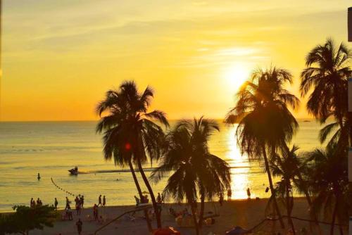 a sunset on a beach with palm trees and the ocean at Apartamento 3 Dormitorios a solo 1 calle del Mar ツ in Puerto de Gaira