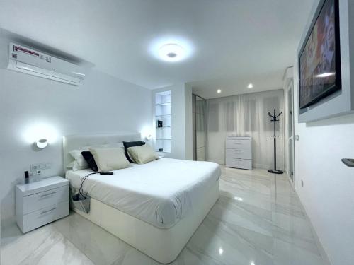 a white bedroom with a large bed and a tv at Apartamento IMPERIO 2 - Marbella centro in Marbella