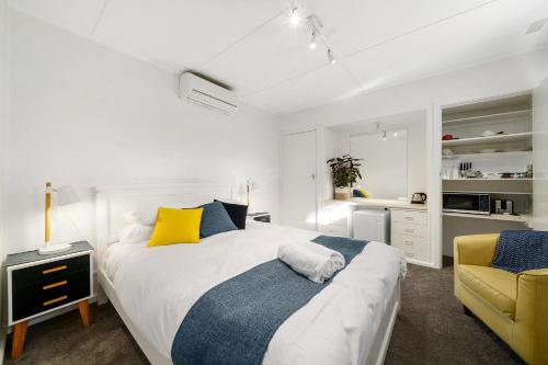 a white bedroom with a bed and a yellow chair at Benson House & Benson Lodge in Benalla