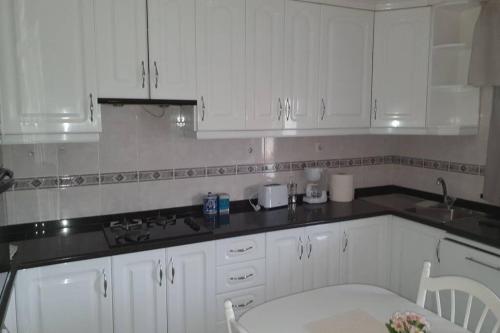 a kitchen with white cabinets and a sink and a table at Paradisíaco. in Moncarapacho