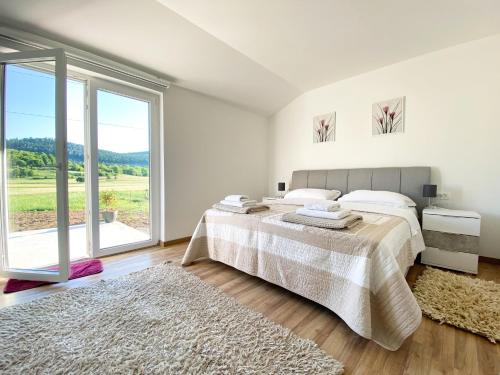 a white bedroom with a bed and a large window at Apartmani Fenestra in Otočac